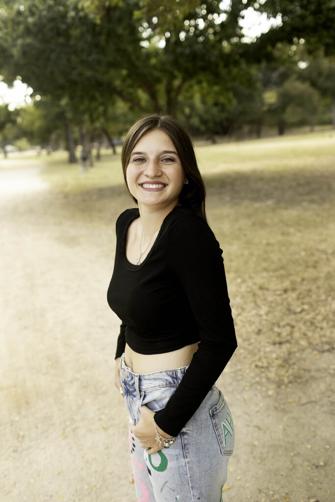 Senior girl standing on a dirt road at Trinity Park, with the sun shining softly on her black shirt and 'Senior 2025' pants