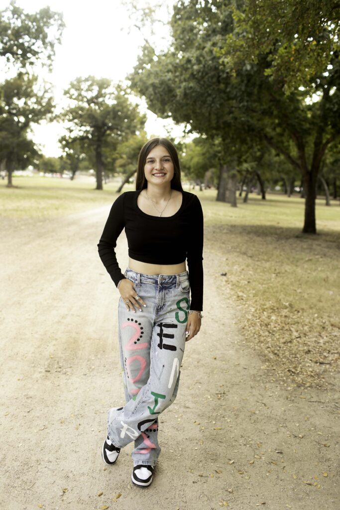 Natural portrait of senior girl on a dirt road in Trinity Park, dressed in a black shirt and 'Senior 2025' pants