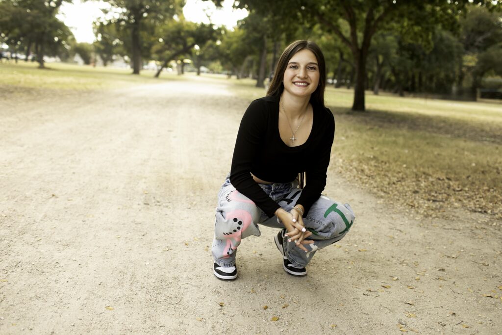 Portrait of senior girl standing confidently on a dirt road at Trinity Park, dressed in a black shirt and 'Senior 2025' pants