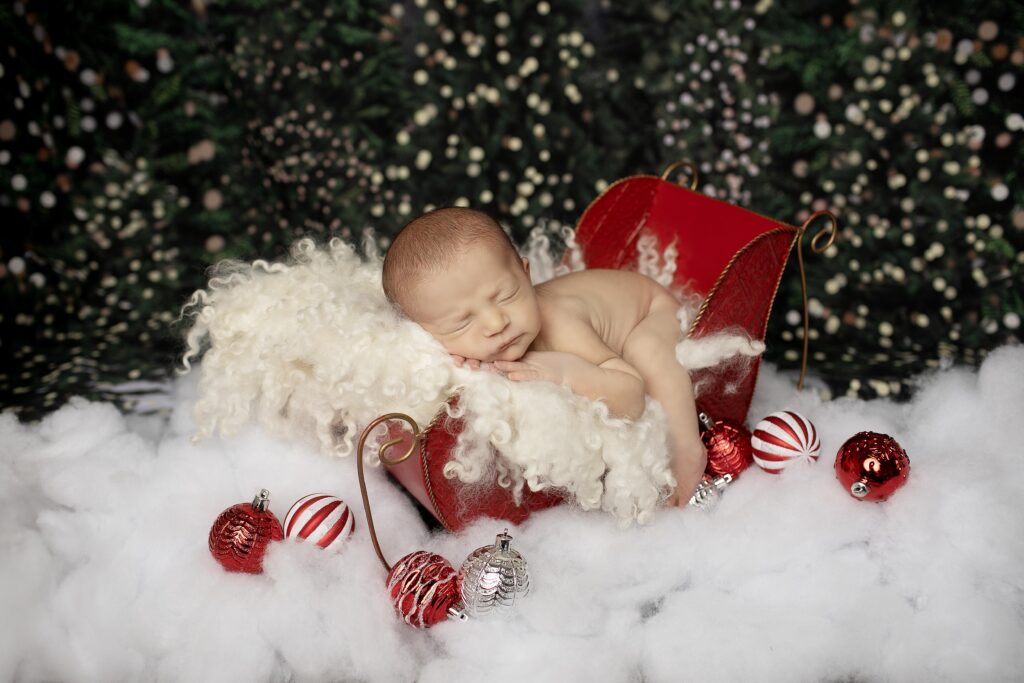 Newborn baby boy peacefully sleeping in a cozy Santa sleigh prop, surrounded by soft blankets and holiday cheer