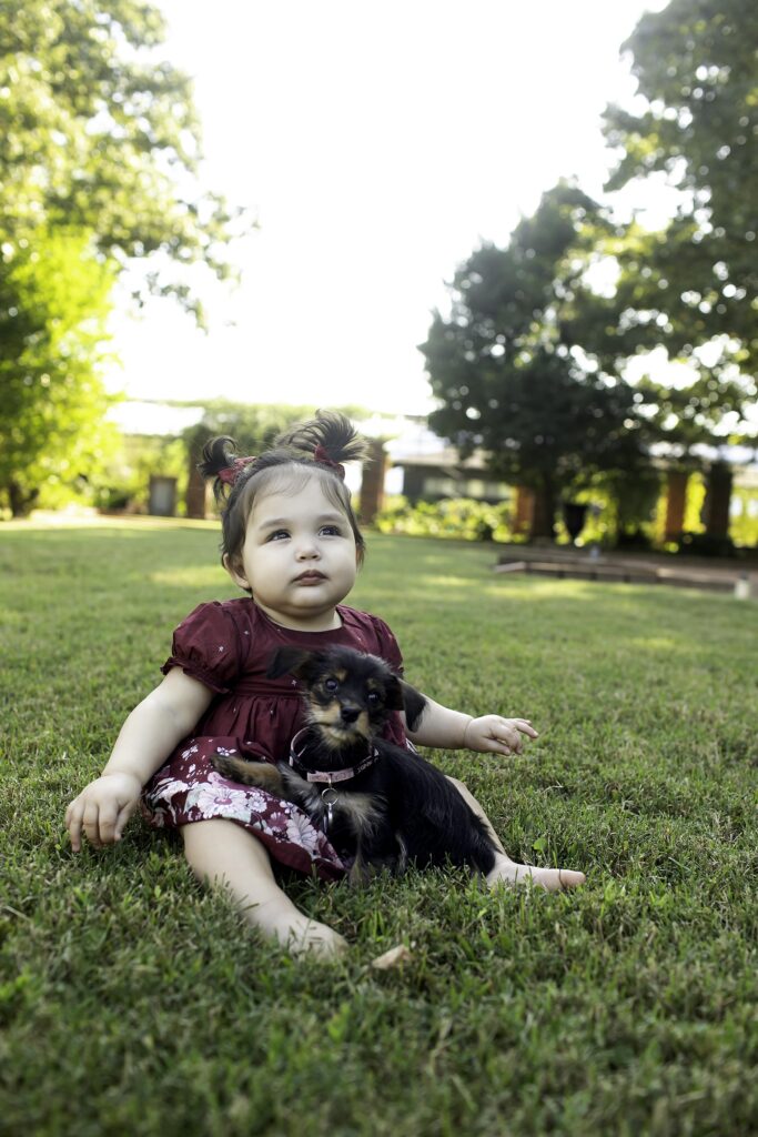 A 1-year-old smiles brightly during their first birthday photoshoot at Clark Gardens in Mineral Wells, TX, surrounded by lush greenery and vibrant flowers