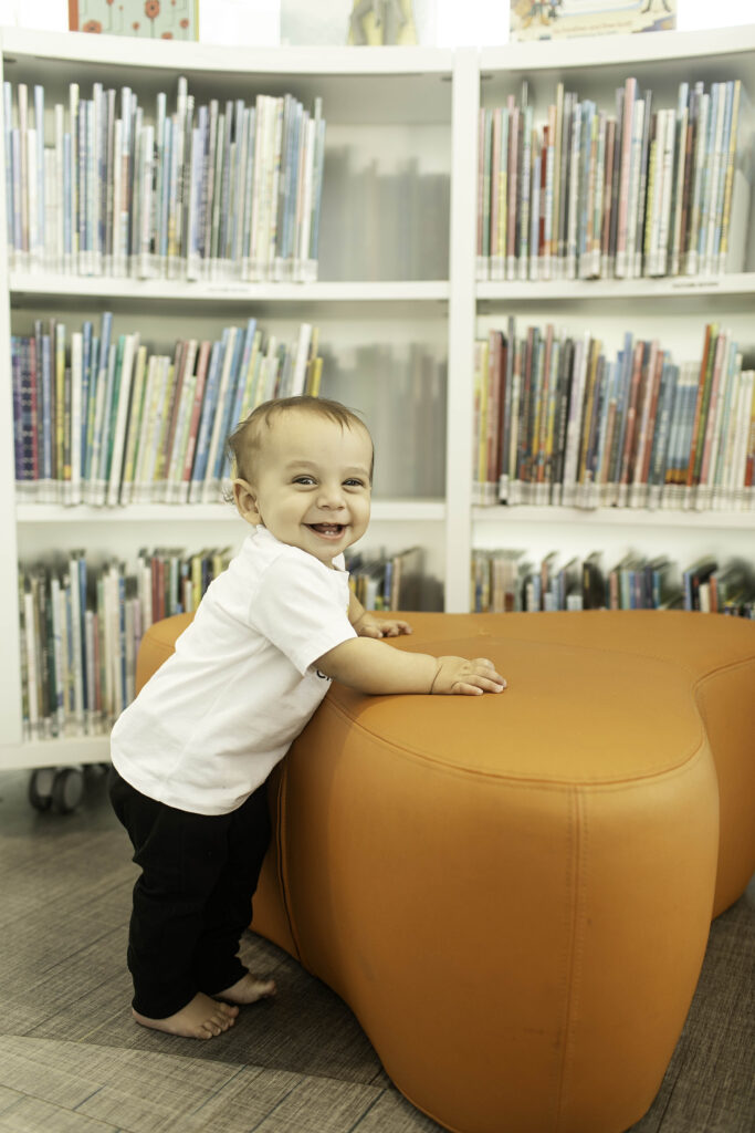 A 1-year-old poses with joy in the Library in Fort Worth, TX, celebrating their first birthday with a photoshoot surrounded by books and meaningful surroundings