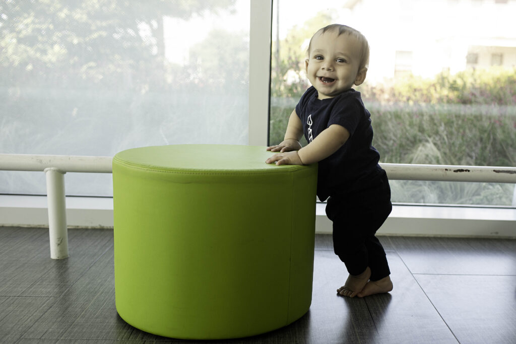 In the Library of Fort Worth, TX, a 1-year-old giggles as they explore during their birthday photoshoot, surrounded by colorful books and a cozy atmosphere.