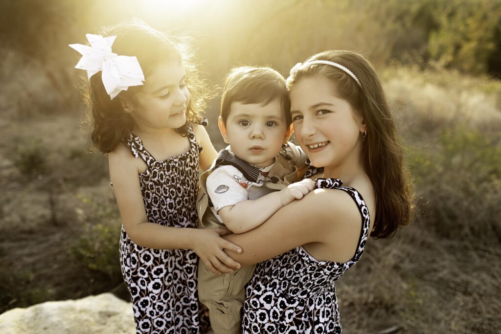 The three sisters gently holding their 6-month-old brother, sharing a sweet moment in nature