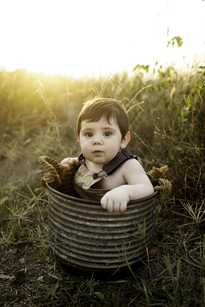 6-month-old boy sitting adorably in a rustic bucket, surrounded by the natural beauty of Tandy Hills