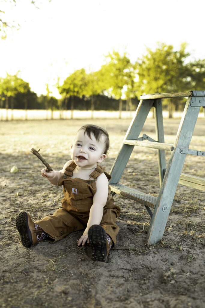 Adorable boy in overalls standing next to a mini ladder, ready for an adventure