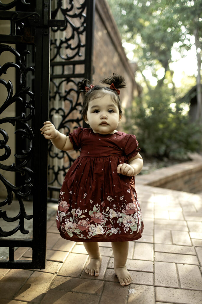 Captured at Clark Gardens in Mineral Wells, TX, a little one smiles for the camera, surrounded by the beauty of blooming flowers and serene greenery