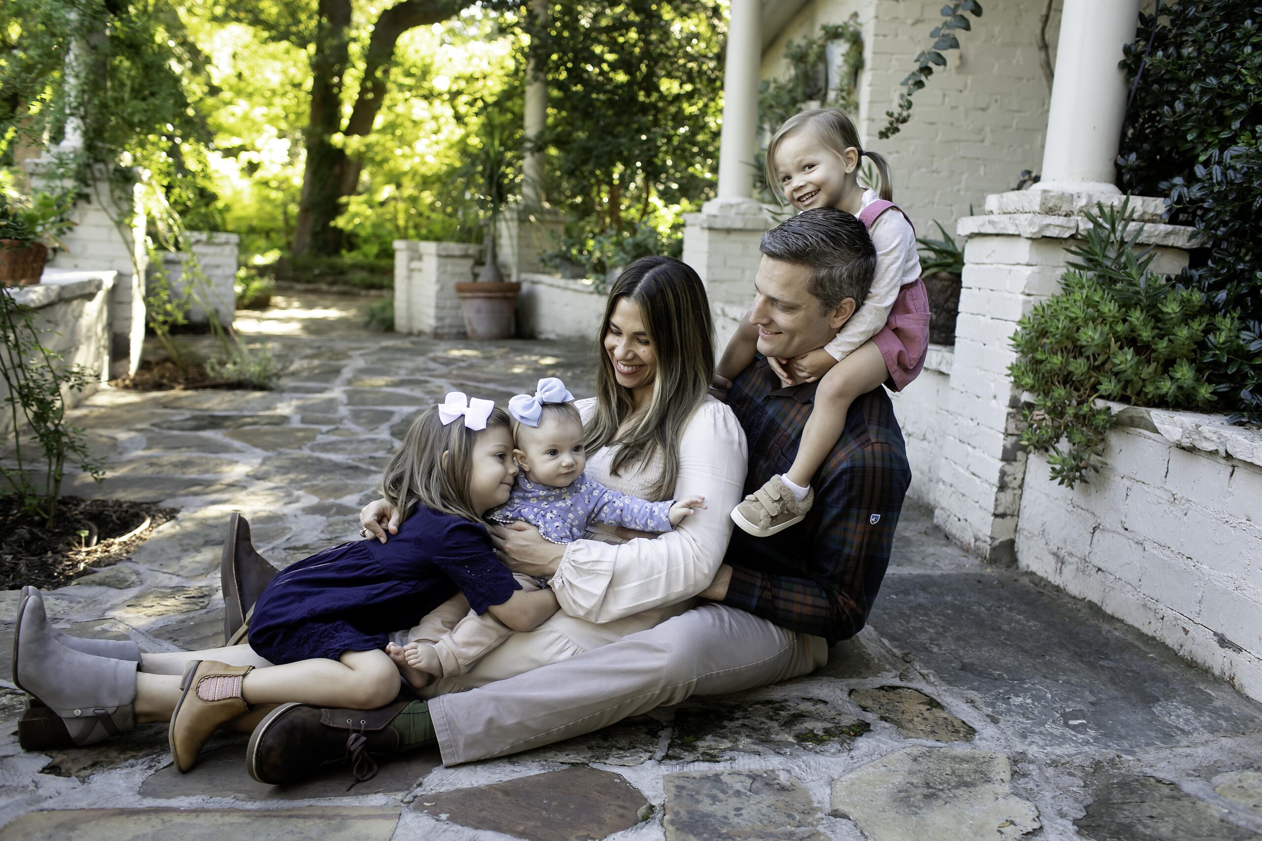 Family portrait session at Chandor Gardens in Weatherford, Texas, featuring a joyful family surrounded by lush greenery, vibrant flowers, and scenic garden landscapes. The group smiles together, capturing precious moments in the serene and picturesque environment, with sunlight streaming through the trees and adding a warm, natural glow to the scene