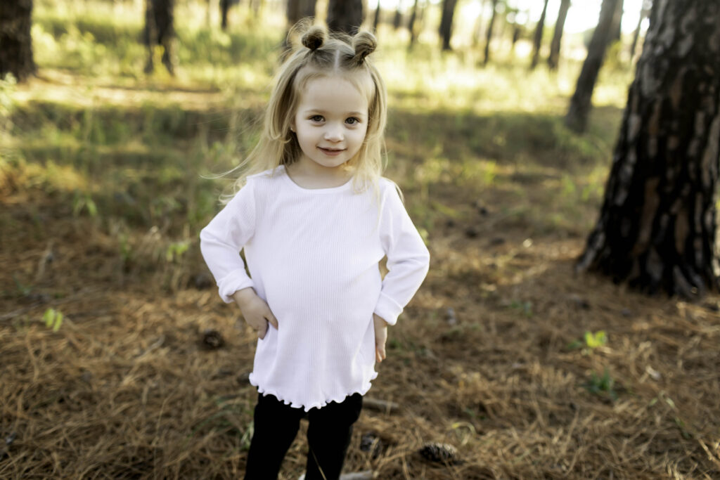 With her hands on her hips and a mischievous grin, big sister shows off her sassy side, standing tall among the towering pine trees in Decatur.