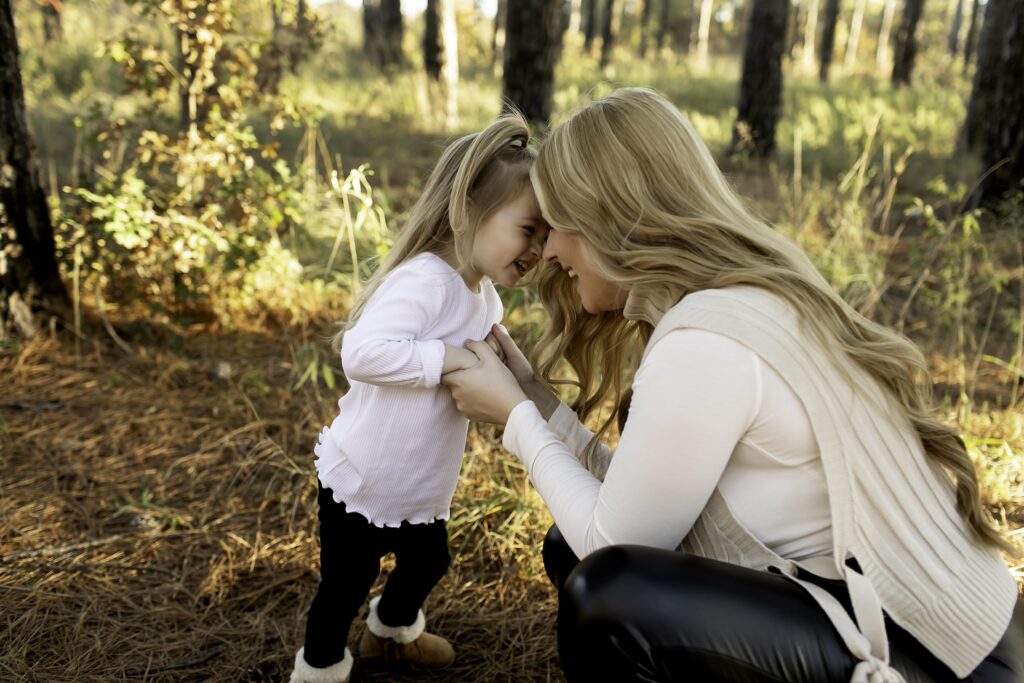 A mom and her 3-year-old share a joyful moment, laughing together among the towering pine trees in Decatur, TX, enjoying the beauty of nature