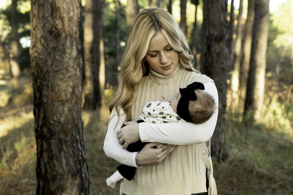 A heartwarming moment as a mom holds her newborn close in the embrace of towering pine trees in Decatur, TX, the soft light filtering through the branches