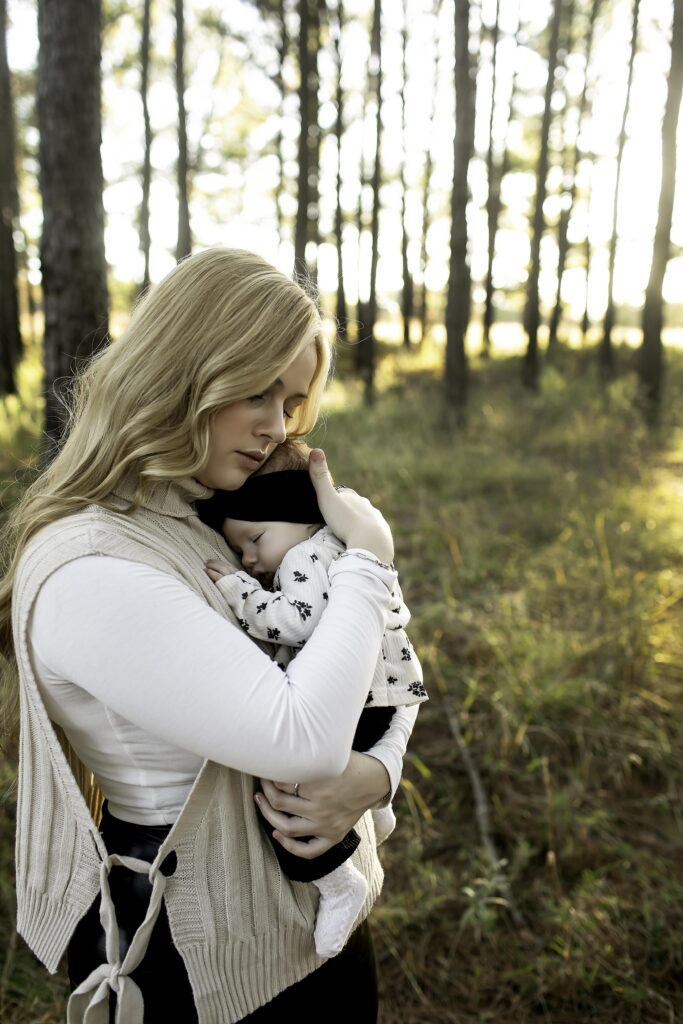 In Decatur’s pine forest, a mother lovingly cradles her newborn, with the towering trees providing a serene backdrop to their special moment together