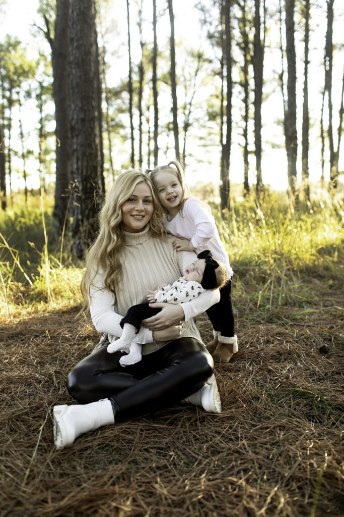 In Decatur’s pine trees, a mom lovingly holds her newborn while giving her 3-year-old a warm hug, creating a tender family moment in nature