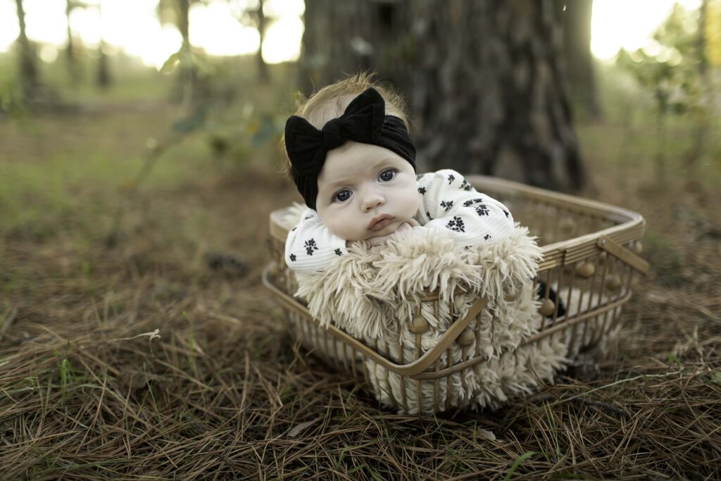 A sweet 2-month-old baby peacefully sleeps in a wicker basket, surrounded by the natural beauty of Decatur’s pine forest, offering a peaceful outdoor moment