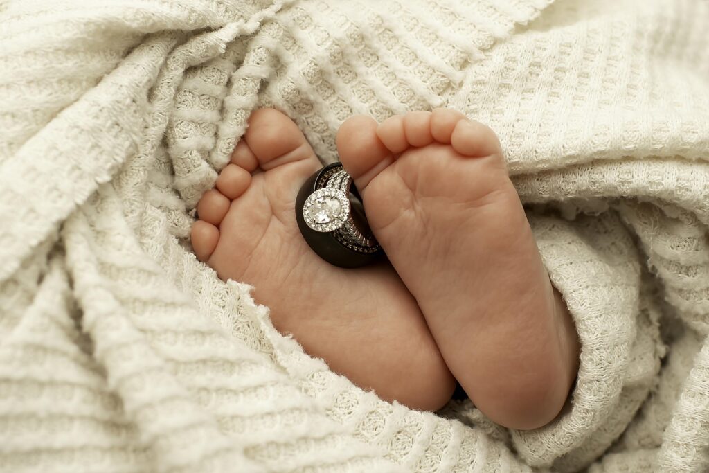 Close-up of newborn baby’s tiny toes with wedding rings gently placed on top, captured during a Chunky Monkey Photography session