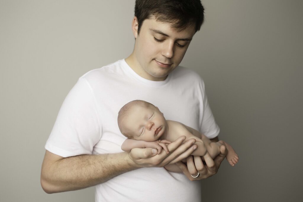 Newborn baby boy cuddled in dad’s arms, creating a sweet and intimate moment during their photoshoot