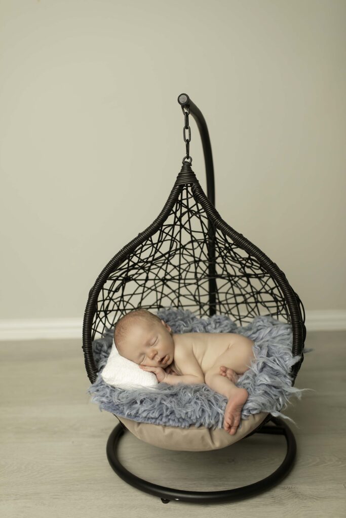 Newborn baby boy peacefully sleeping in a hanging basket, surrounded by soft, cozy fabrics