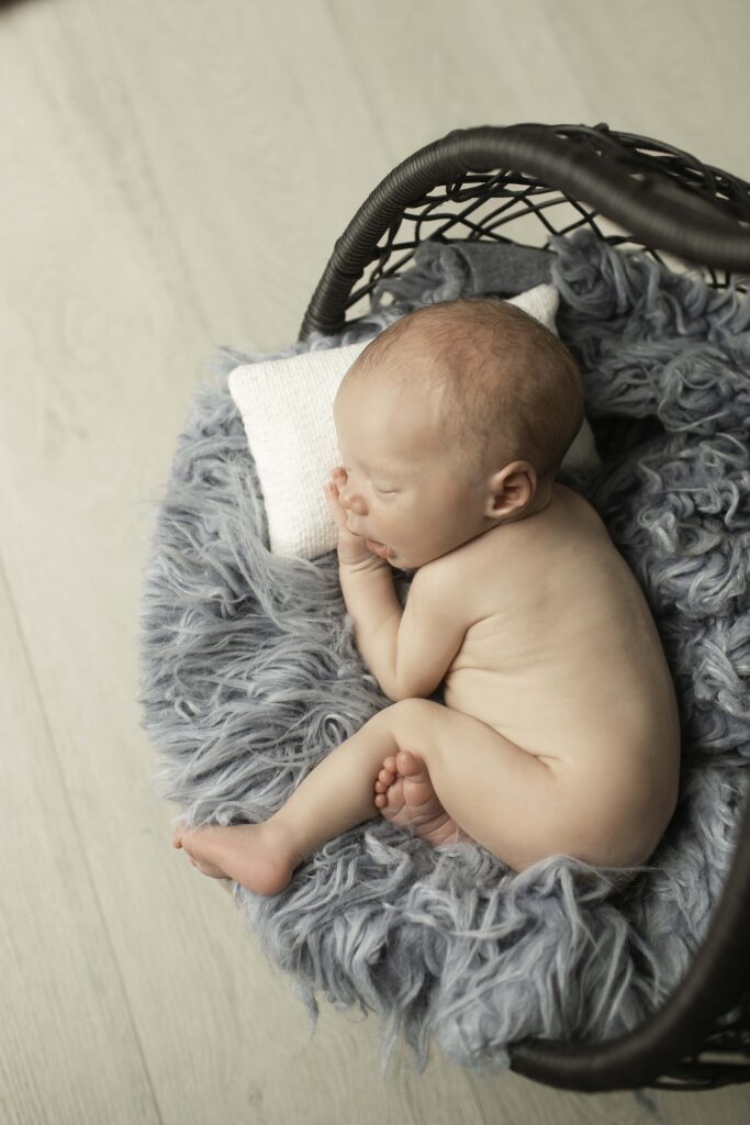 Adorable newborn boy curled up in a hanging basket, wrapped in a soft blanket for a peaceful moment.