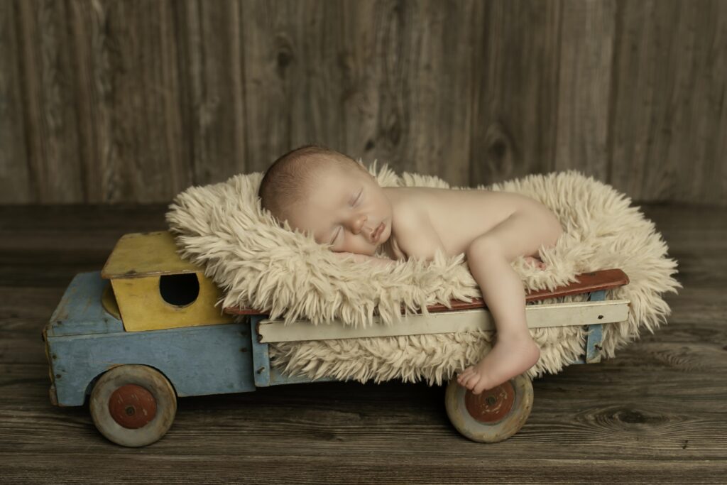 Adorable newborn boy curled up in a vintage truck prop, adding a charming touch to his session