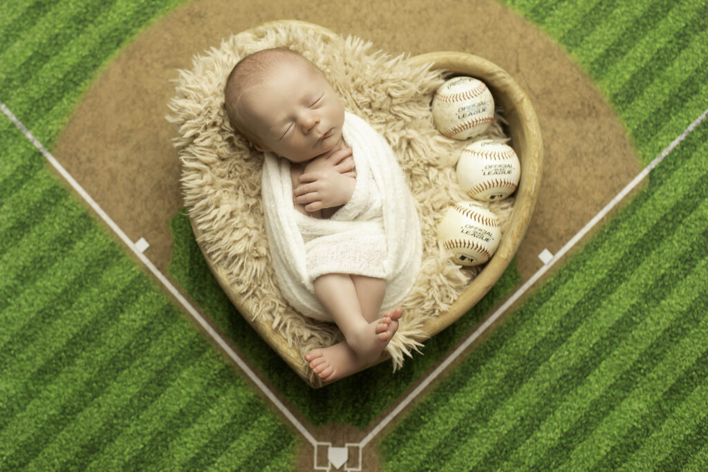 Newborn baby peacefully resting inside a heart-shaped prop, with a baseball-themed backdrop, captured during a Chunky Monkey Photography session