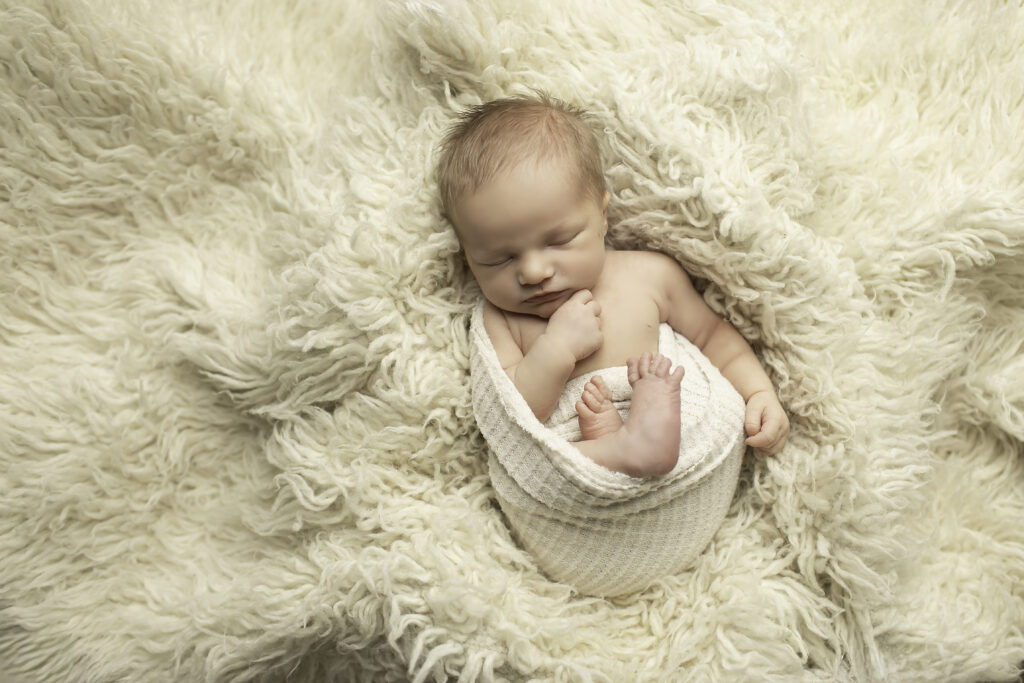 Newborn baby snuggled in a soft, knitted wrap, surrounded by gentle lighting and soft colors in the studio