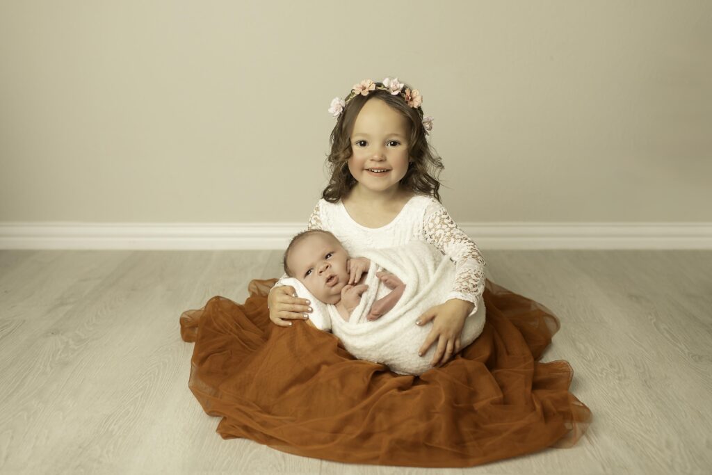 Each sister gently holding her newborn brother, capturing a sweet and personal moment between siblings