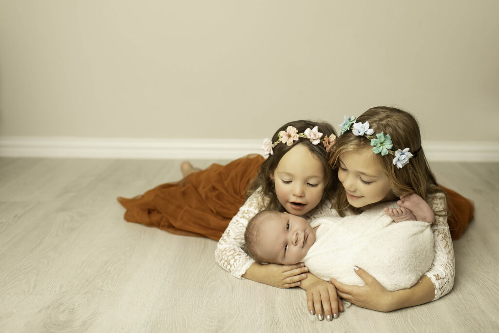 Sisters lovingly gazing at their newborn brother, sharing a sweet moment of sibling connection