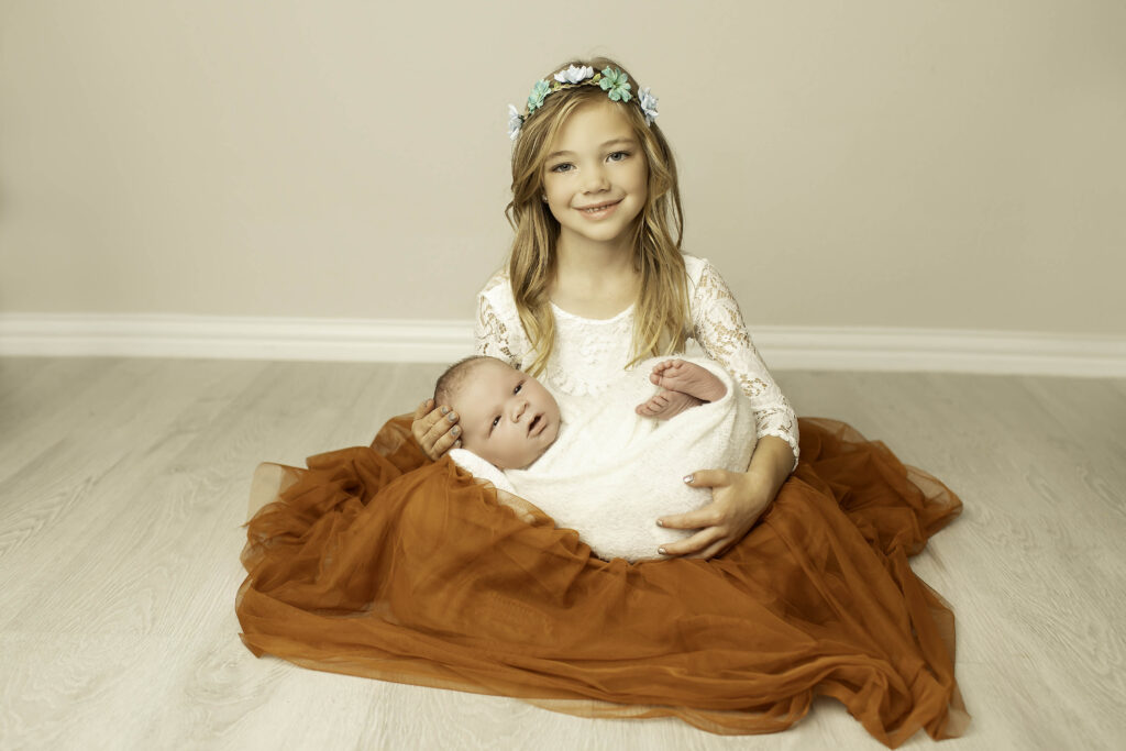 Each sister gently holding her newborn brother, capturing a sweet and personal moment between siblings