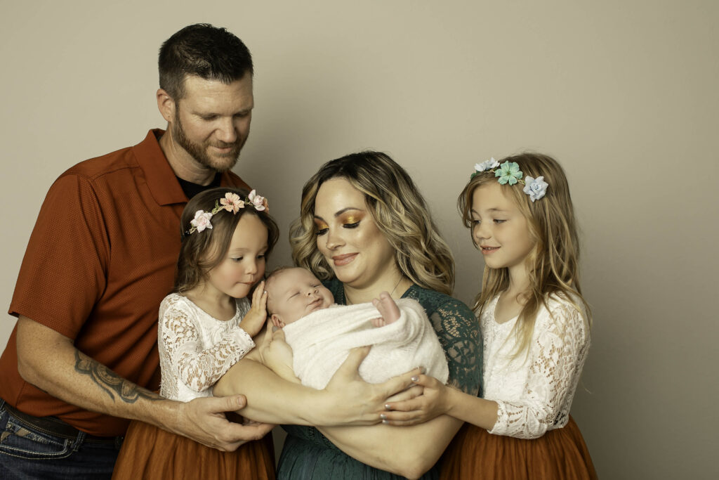 Family of four smiling together, with parents holding their newborn boy in a warm and loving moment