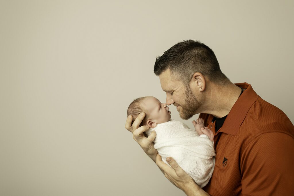 Dad and newborn boy nose-to-nose, sharing a tender, loving moment captured in a heartwarming family photo