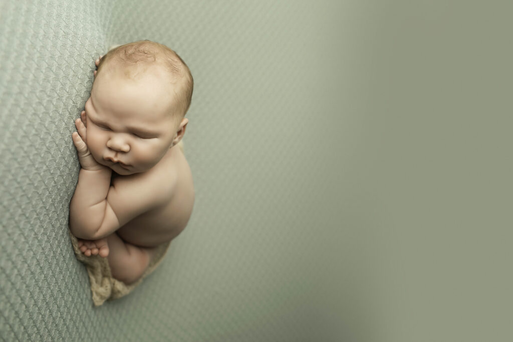 Newborn boy wrapped in a neutral-toned swaddle, lying comfortably on a soft blanket