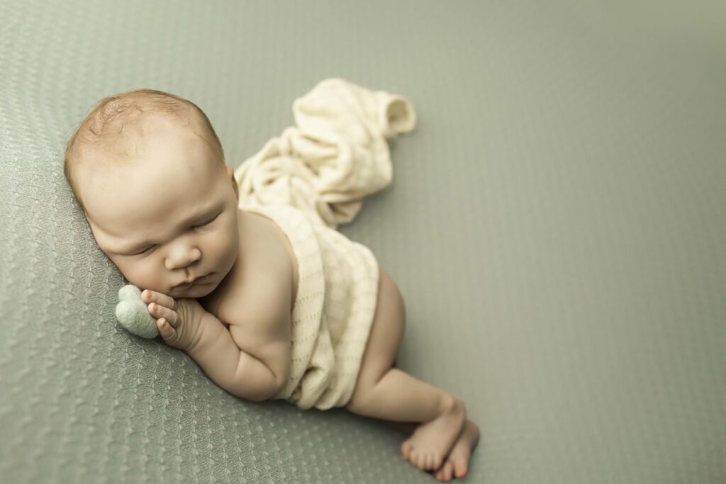 Adorable newborn boy curled up in a soft swaddle, resting peacefully in the studio