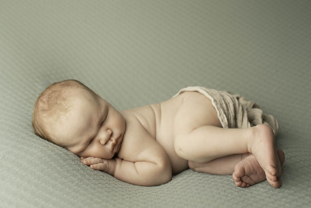 Newborn boy lying on a soft blanket, surrounded by neutral-toned props for a serene photoshoot