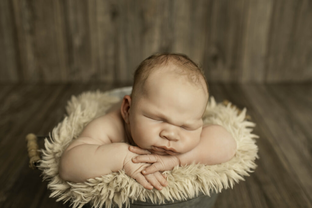 Newborn boy sleeping soundly in a cute, rustic bucket, creating an endearing and peaceful moment