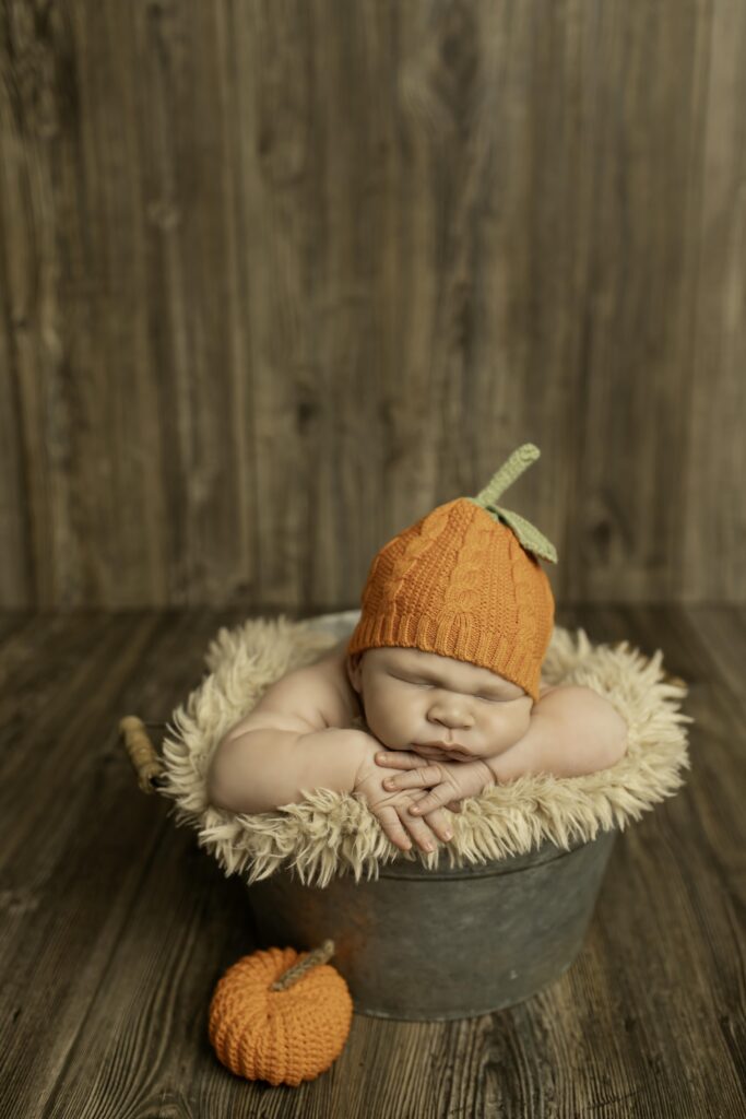 Newborn boy peacefully resting in a rustic bucket, wrapped in a soft blanket for a cozy, serene photo