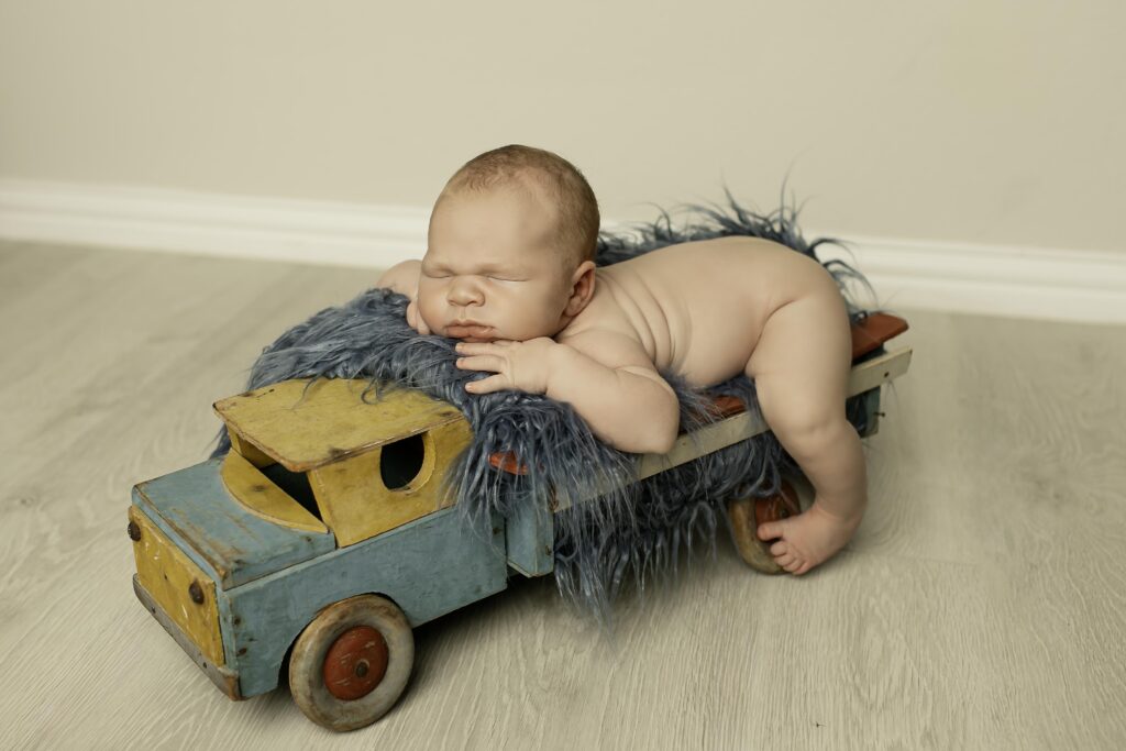 Newborn boy peacefully sleeping in a vintage truck prop, surrounded by cozy blankets for a charming photoshoot