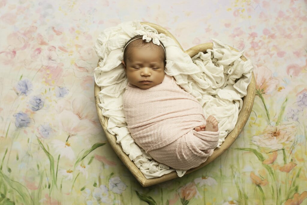 Newborn girl nestled in a heart-shaped prop, wrapped in a cozy blanket, creating a sweet moment in the studio