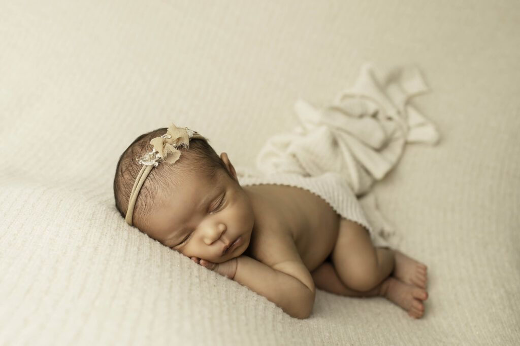 Adorable newborn girl posed simply on a soft, neutral backdrop, creating a serene and timeless studio portrait