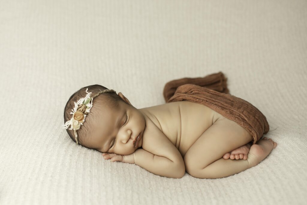 Adorable newborn girl posed gently on a neutral backdrop, showcasing her tiny features in a minimalist studio shot