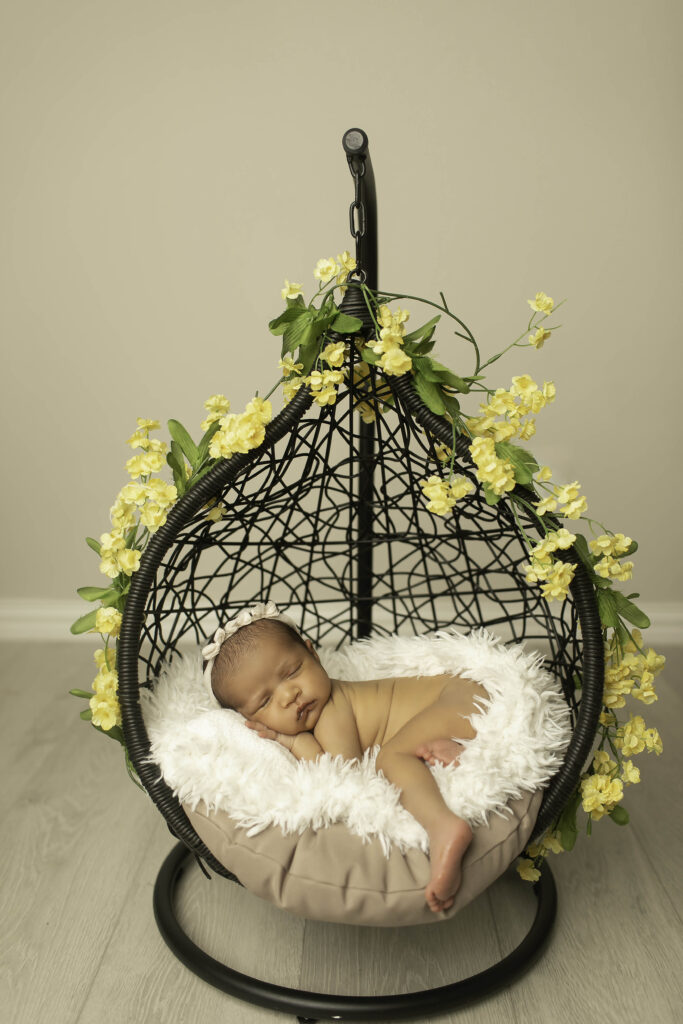 Sweet newborn girl comfortably nestled in a hanging basket, framed by beautiful yellow flowers in the studio