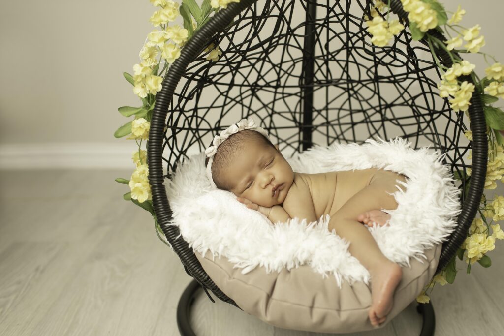 Adorable newborn girl lying in a hanging basket, with vibrant yellow flowers adding a pop of color