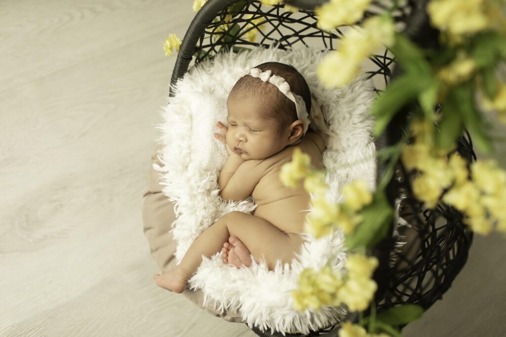 Newborn girl peacefully resting in a hanging basket, surrounded by soft yellow flowers in the studio