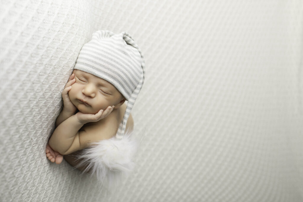 Newborn baby boy gently resting on a soft, textured blanket with a cute hat, in a studio environment