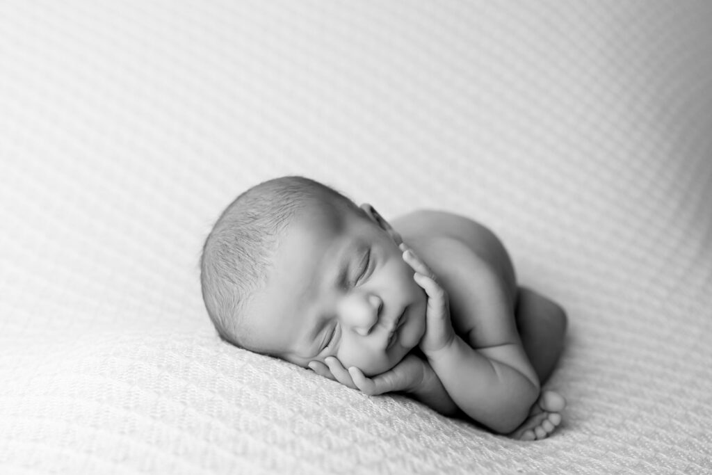 Newborn baby boy with a serene expression, posed in a studio setup with soft lighting