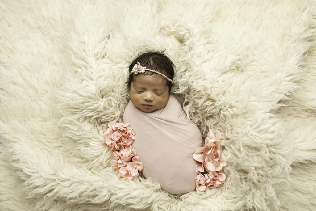 A newborn girl, wrapped in a soft blanket, peacefully sleeps surrounded by delicate flowers in a serene Fort Worth studio, creating a tranquil and beautiful scene