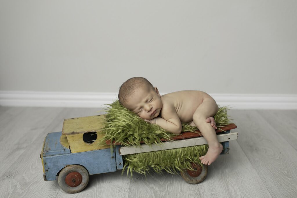 Newborn baby boy peacefully sleeping in a cute truck prop, surrounded by soft blankets