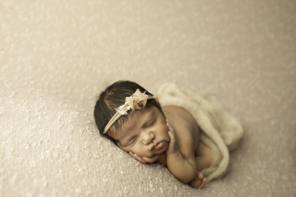 A newborn girl is wrapped in a soft, neutral blanket, lying peacefully in a Fort Worth studio, creating a tender and timeless portrait