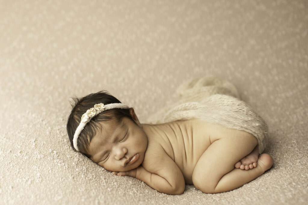 In a soft, neutral-toned blanket, a newborn girl sleeps soundly in a Fort Worth studio, creating a timeless and simple portrait of her early days