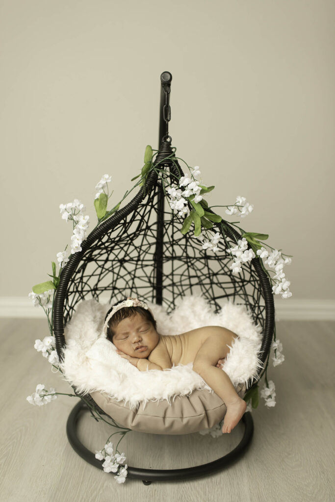 Newborn baby peacefully sleeping in a hanging basket, surrounded by soft fabrics and gentle props during a Chunky Monkey session