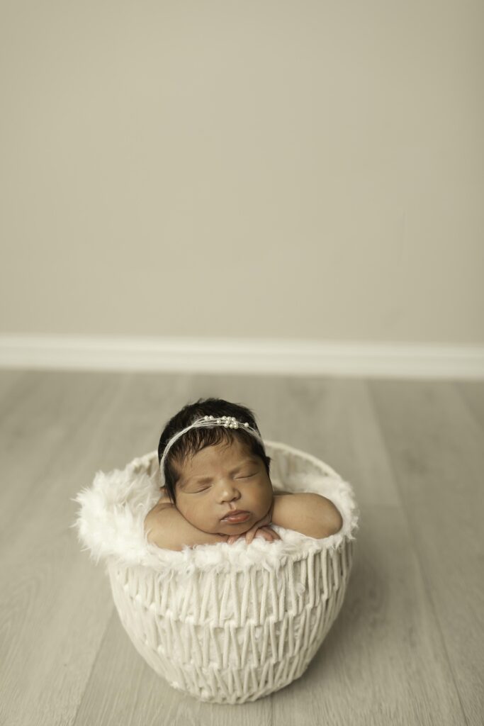 A newborn girl lies gently in a white basket, her tiny hands peeking out, creating a heartwarming image of serenity and beauty in a Fort Worth studio